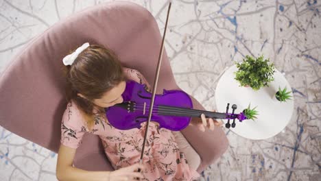 Young-girl-sitting-on-sofa-in-living-room-playing-violin.-Musicianship.